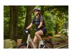 Woman cycling on an e-bike in a park, wearing a helmet, sunglasses, and sportswear.