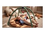 Baby on a playmat with an activity arch, surrounded by pillows and a teddy bear.