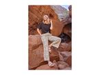 Woman in a black t-shirt and patterned trousers, posing on rocks in a canyon.