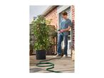 Man watering a potted tomato plant with a hose on a wooden deck.