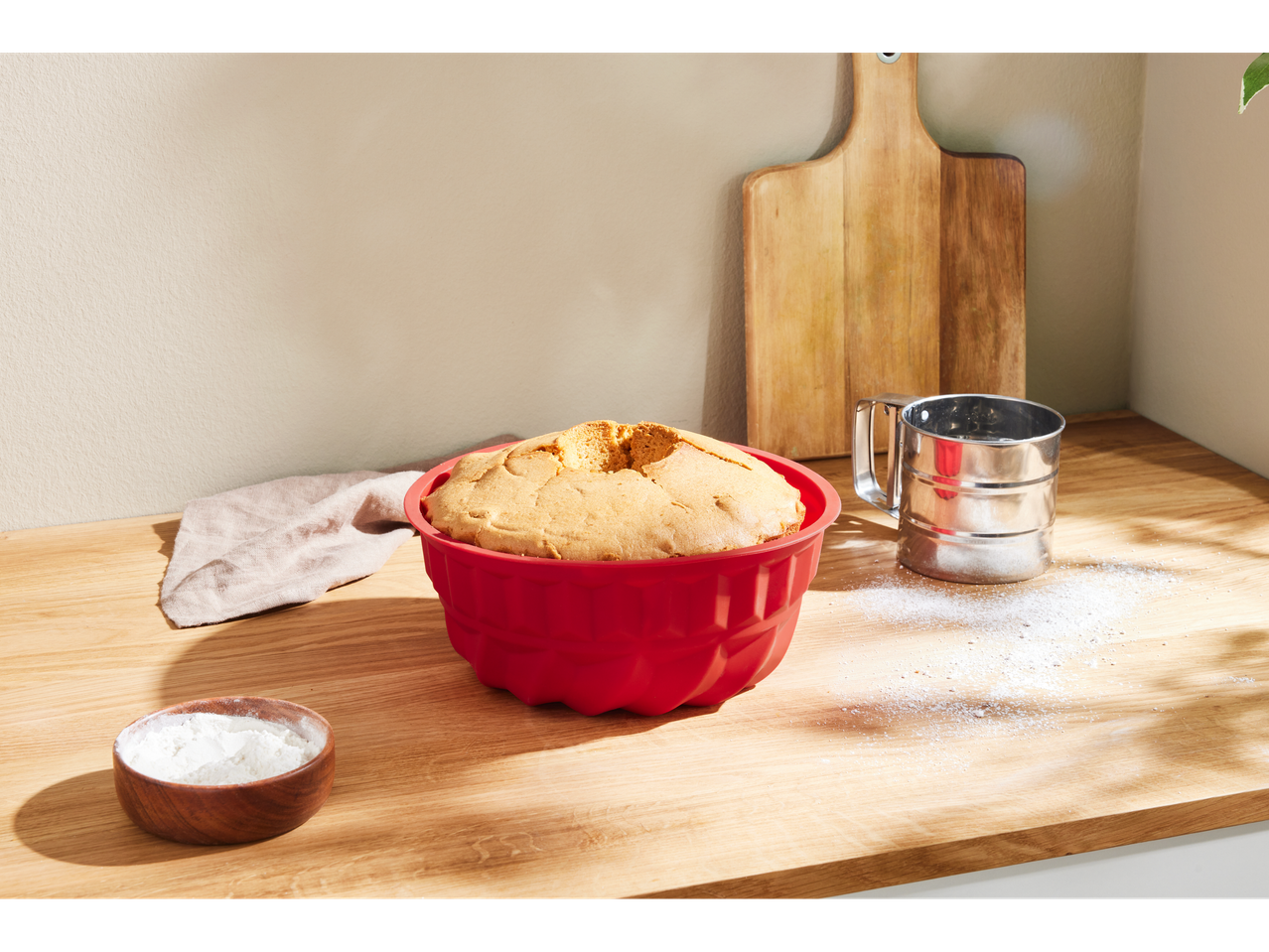 A baked cake in a red SILVERCREST® silicone mold on a wooden counter with flour.