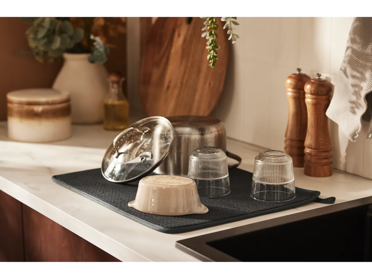 Utensílios de cozinha e copos em um tapete de secagem cinza escuro.