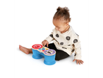 A baby plays with a blue and red Hape musical instrument.