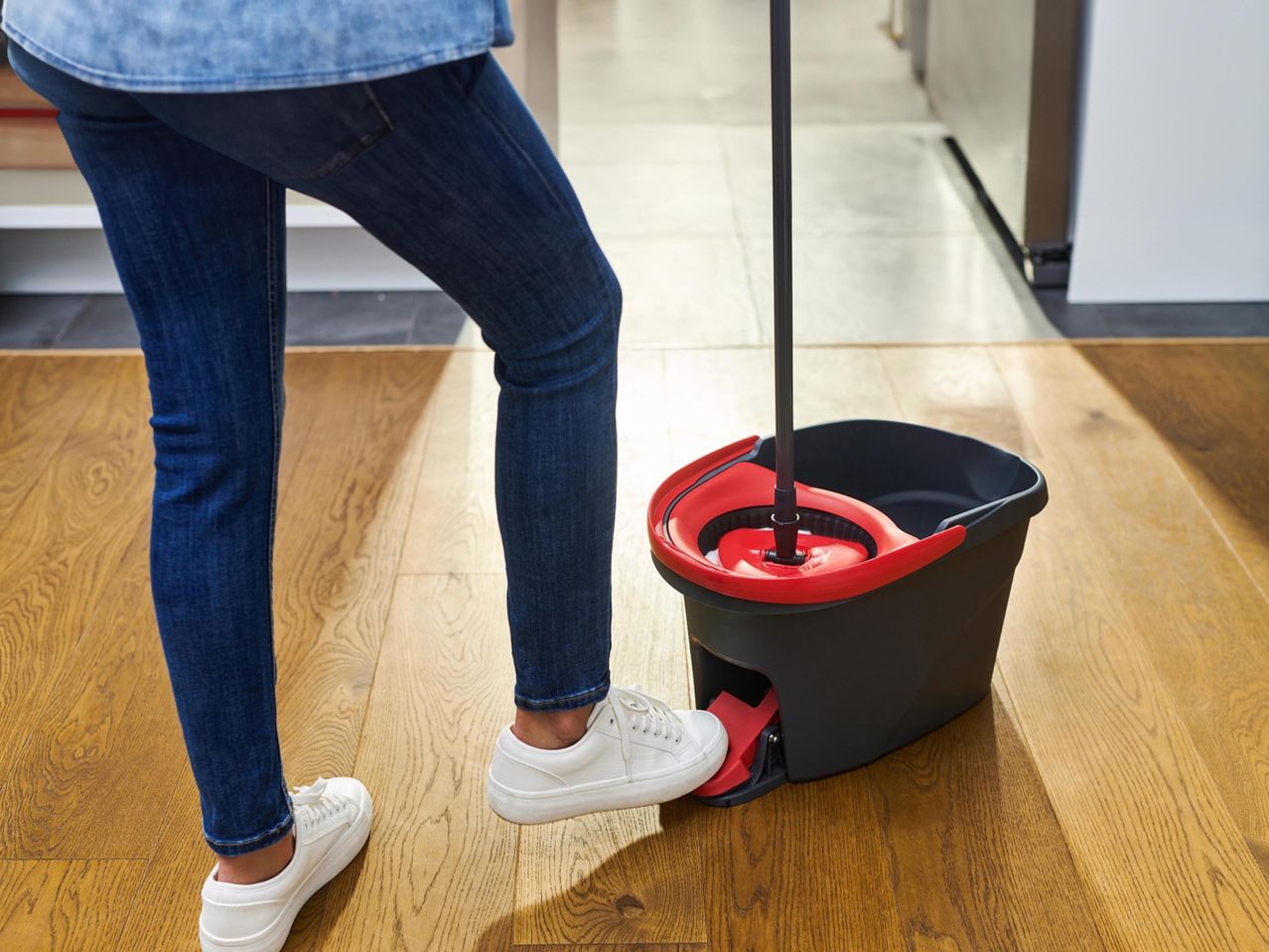 Nő takarít felmosóval és vödörrel, lábával a pedálon.