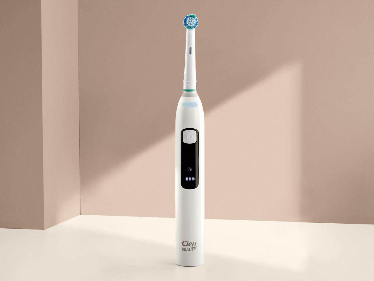 A white electric toothbrush with a blue and green brush head stands upright against a beige background.