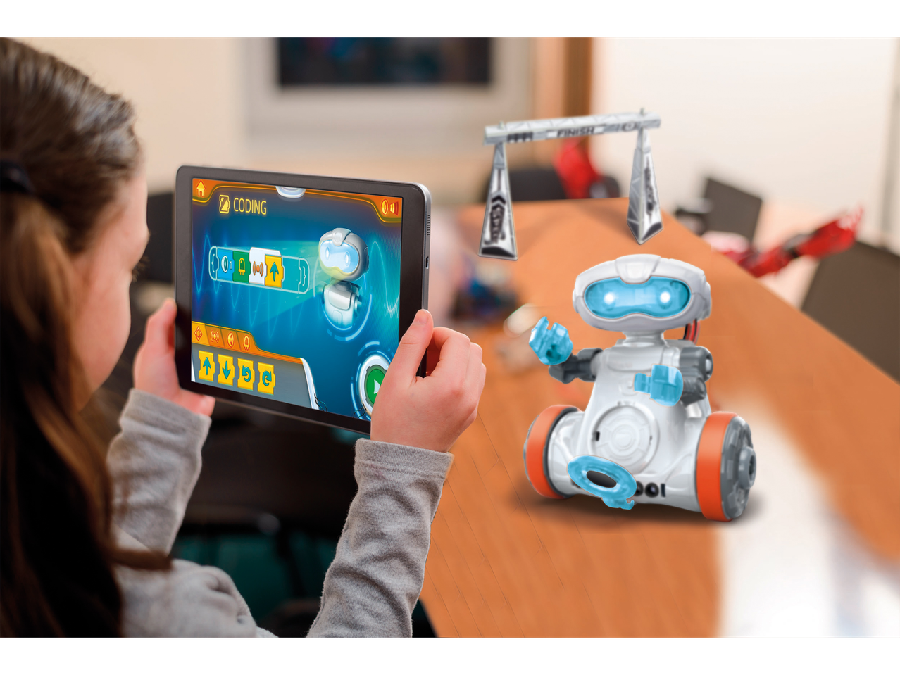 Dijete programira robota na tabletu, s robotom i ciljnom linijom na stolu.