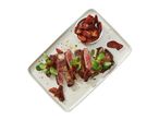 Sliced steak with sun-dried tomatoes and lamb's lettuce on a rectangular plate.