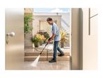 Man pressure washing outdoor patio tiles and steps with a high-pressure cleaner.
