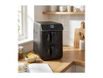 Black dual-basket air fryer on a wooden kitchen counter with a cookbook and ingredients.