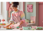 Uma mulher assa bolos em uma cozinha rosa pastel usando uma forma de bundt cake.