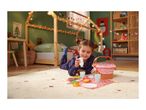 Girl playing with a toy picnic basket and food on a rug in a Christmas-themed room.