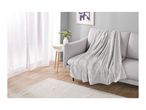 A light gray sofa with a textured throw blanket, a white side table with a vase of flowers, and a white rug.