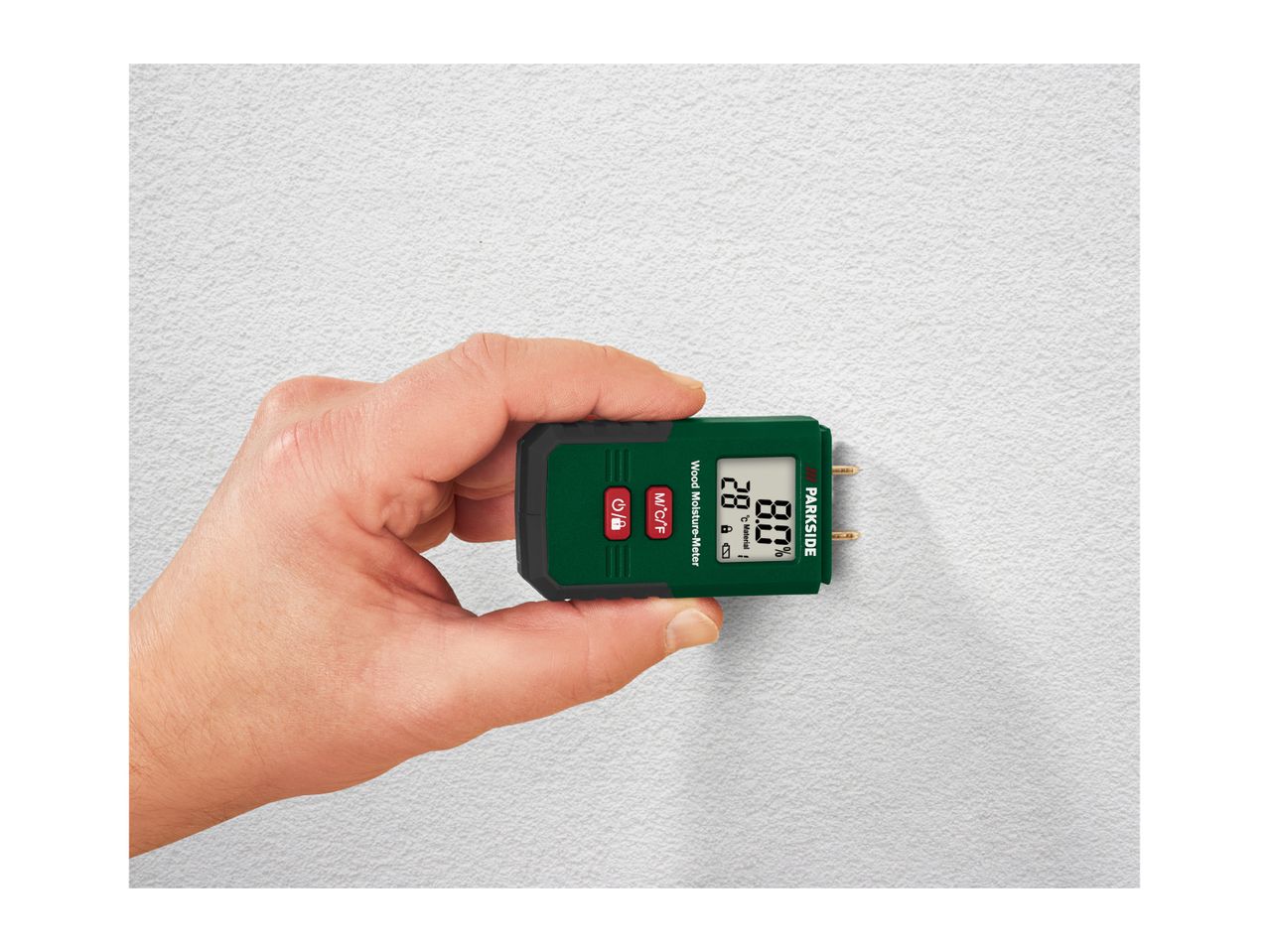 Hand holding a wood moisture meter against a white textured wall, displaying 28°C and 8.0% moisture.