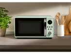A mint green SilverCrest retro microwave sits on a countertop with wooden utensils and a plant.