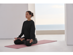 Woman meditating on a CRIVIT Yoga Mat, wearing black activewear, with a sea view.