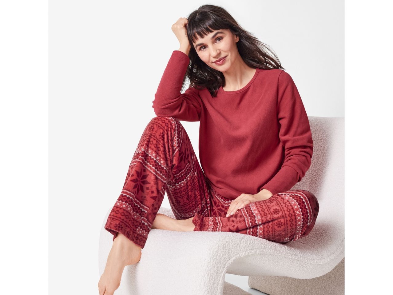 Woman in red fleece pajamas with a festive pattern, sitting on a white chair.