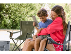 Woman and child sitting on camping chairs, looking at a notebook, with a cooler bag nearby.