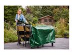 Woman covering outdoor furniture with a green protective tarp in a garden setting.
