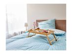 Breakfast in bed with a wooden tray, blue striped bedding, and a bedside lamp.