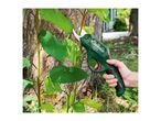 Hand holding green electric pruning shears to cut a small branch from a tree.