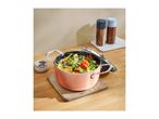 A copper-colored pot filled with colorful vegetables on a wooden board, with salt and pepper shakers nearby.