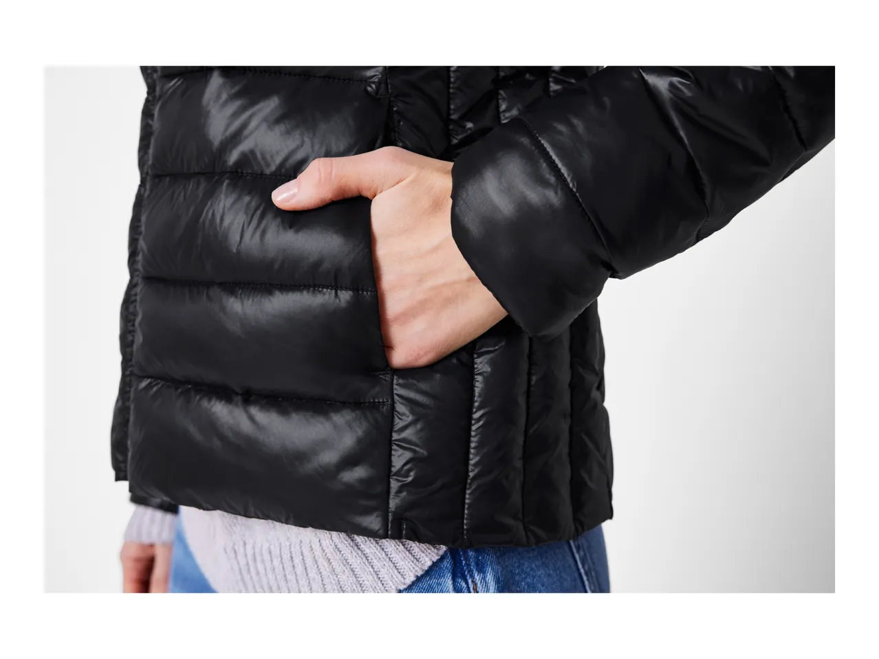 A person wearing a black puffer jacket with their hand in the pocket.