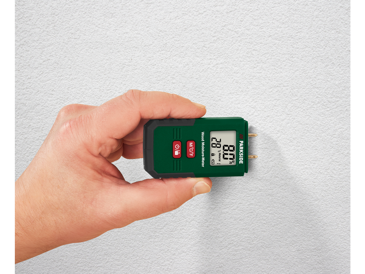 Mão segurando um medidor de humidade de madeira contra uma parede branca texturizada, exibindo 28°C e 8,0% de humidade.