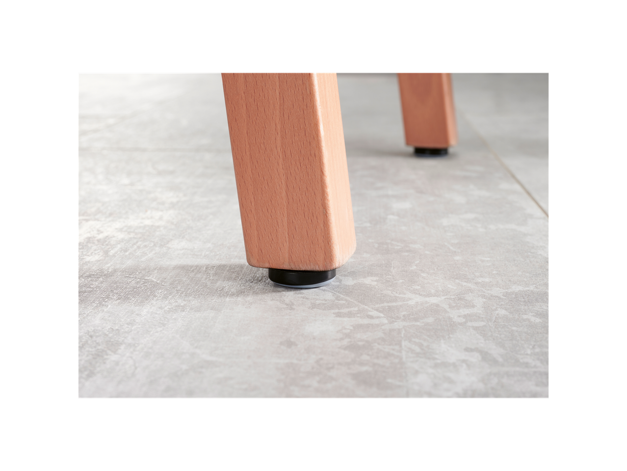 Close-up of light wood furniture legs with black protective floor glides on a light gray floor.