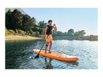 Man on a stand-up paddleboard with a paddle on a lake surrounded by trees and mountains.