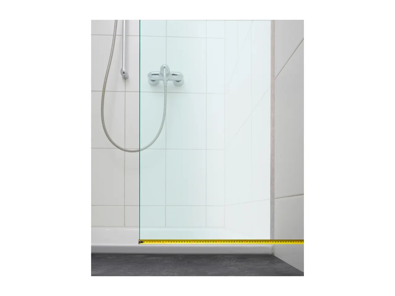 A shower stall with a glass door and a measuring tape on the floor showing the width.