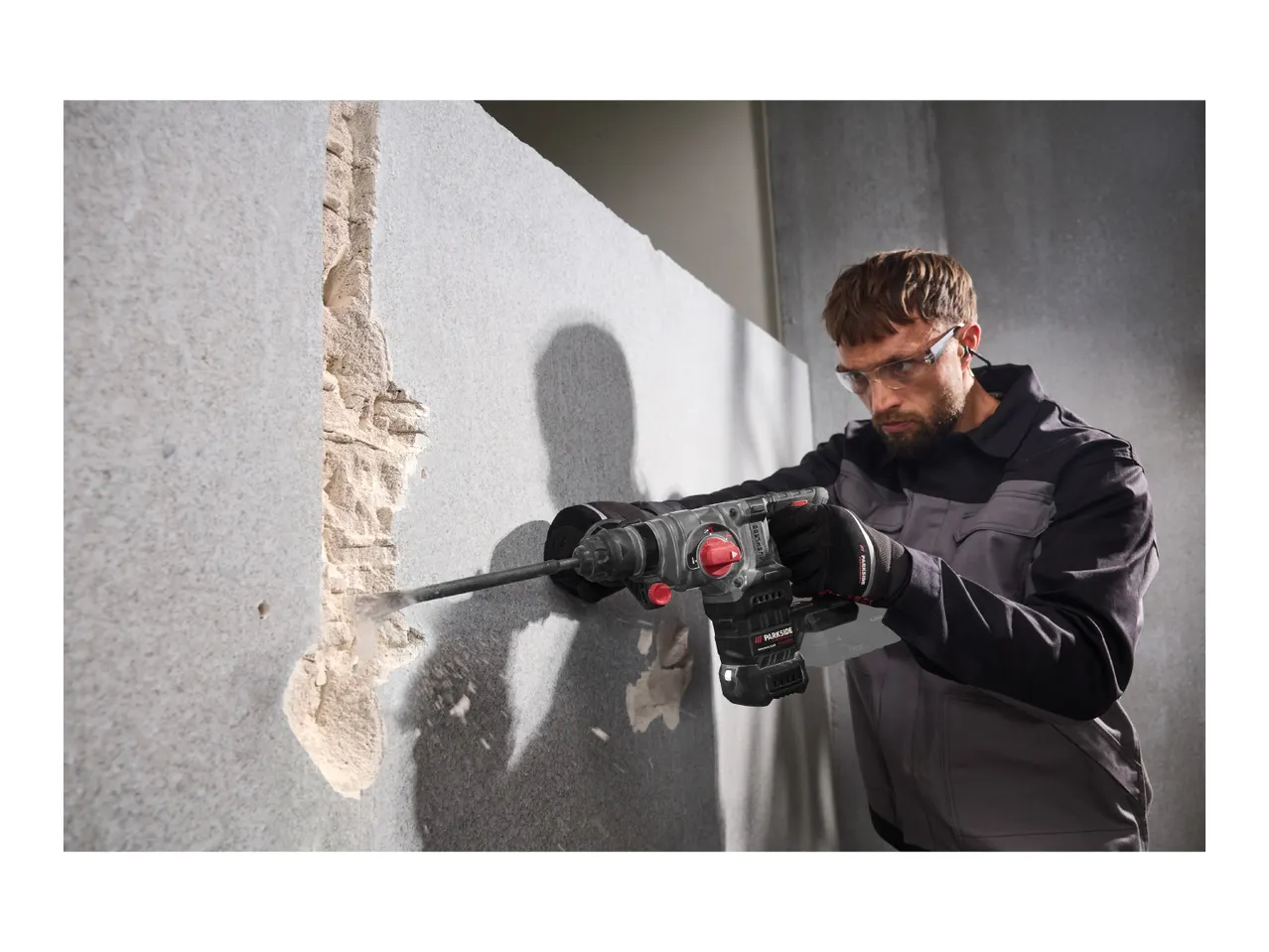 A man using a cordless rotary hammer to chisel a concrete wall.