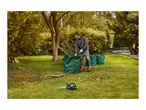 Man in garden clearing branches into green garden waste bags with a chainsaw nearby.