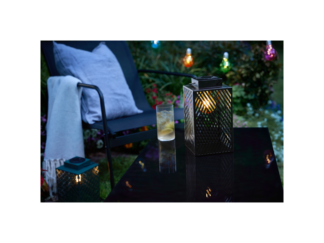 Solar lanterns and a drink on a table in a garden at evening.