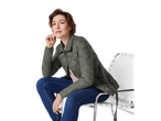 Donna in giacca trapuntata leggera e jeans, seduta su una sedia.