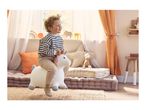 Happy child on a unicorn bouncy toy in a bright, cozy playroom with floor cushions.