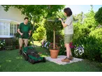 Man mowing lawn and woman trimming topiary in a sunny garden.