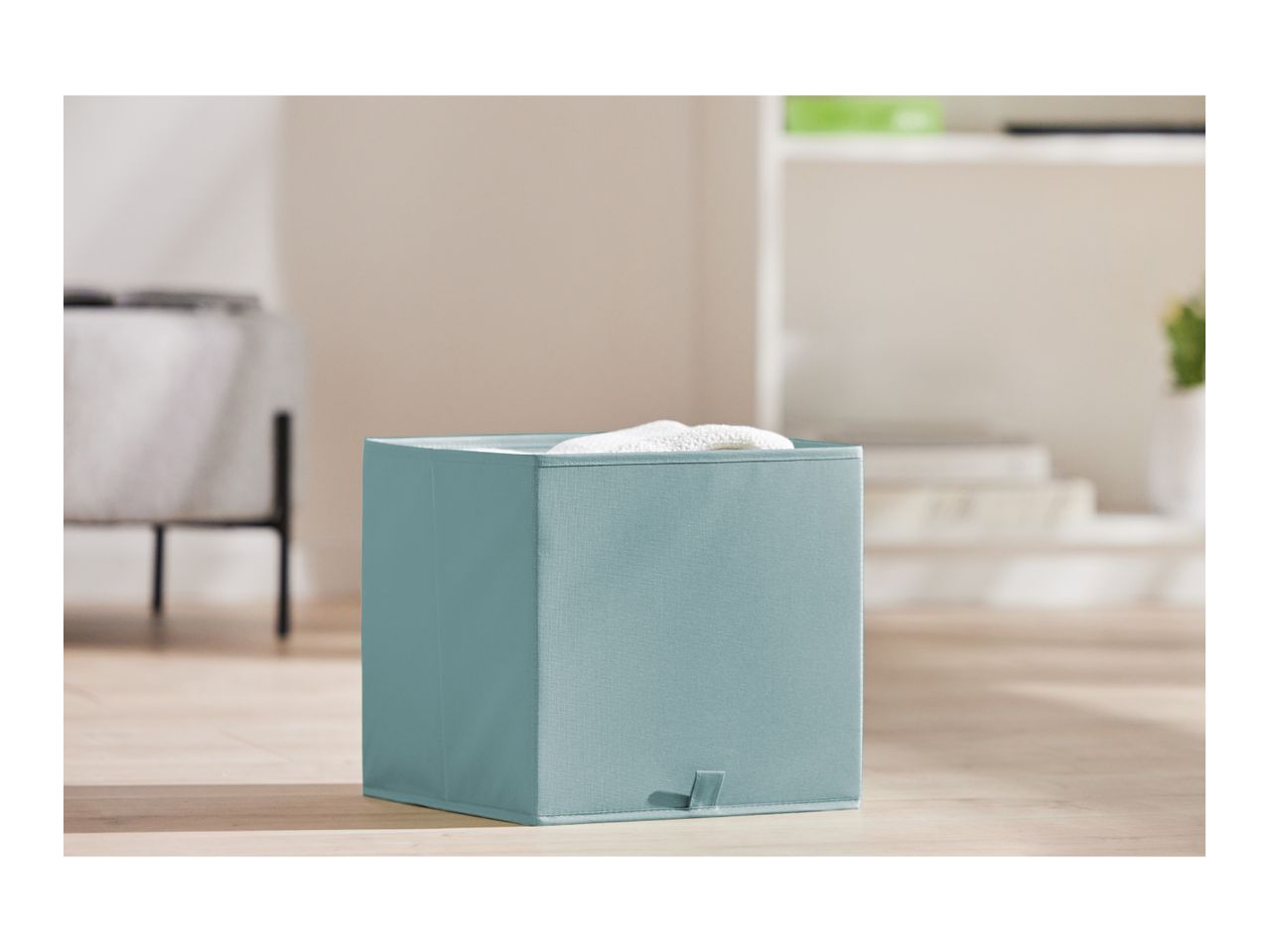 Light blue fabric storage cube with a white towel inside, on a wooden floor.