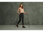 A woman in a beanie, long-sleeved shirt, and leggings, holding trekking poles.
