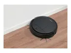 Black robotic vacuum cleaner on a wooden floor next to a white wall.