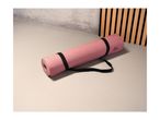Pink Crivit yoga mat with a black strap on a light floor.