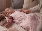 Baby in a pink star-patterned sleeping bag, with a hand adjusting it in a crib.