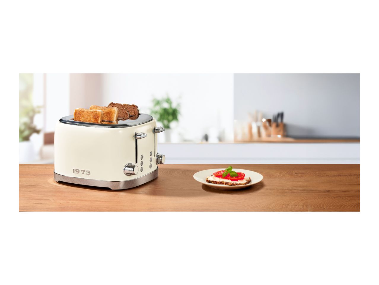 Retro-style 4-slice toaster with '1973' lettering on a wooden table next to a plate of toast.
