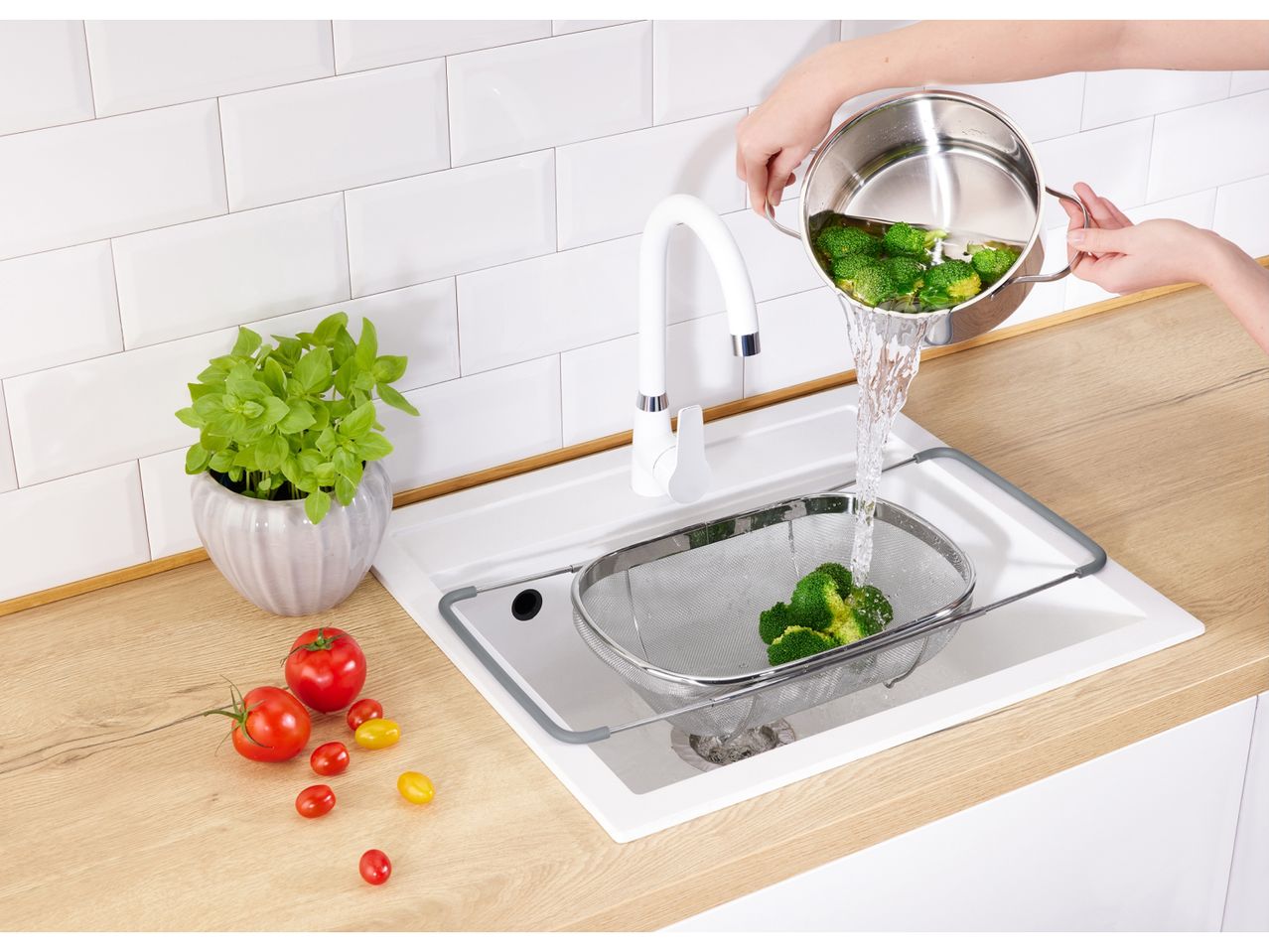 Stainless steel Extendable Sieve in a kitchen sink, being rinsed with water.