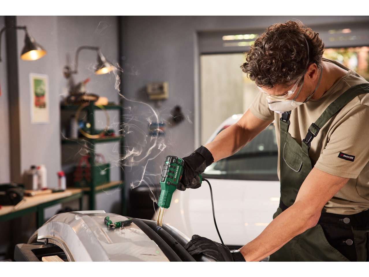 Bărbat cu mască și ochelari de protecție, folosind un pistol de sudură PARKSIDE pentru plastic.
