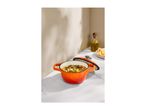 Orange cast iron pot with stew, olive oil, and chopped vegetables on a marble counter.