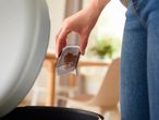 A person holding a used coffee pod over a trash can.