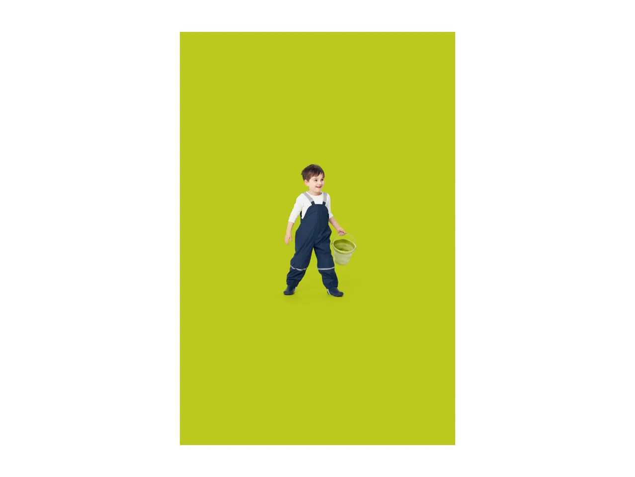 Toddler in navy waterproof dungarees and white long-sleeve top, holding a green bucket.