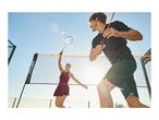 Two people playing badminton outdoors, one hitting a shuttlecock over the net.