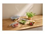Glass food containers with fresh vegetables and fruit on a wooden kitchen counter.