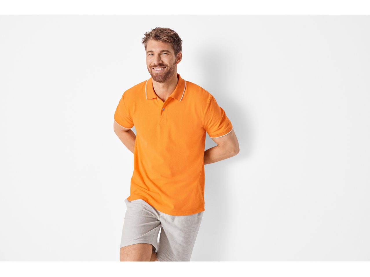 Bărbat zâmbitor îmbrăcat cu un polo portocaliu și pantaloni scurți gri.